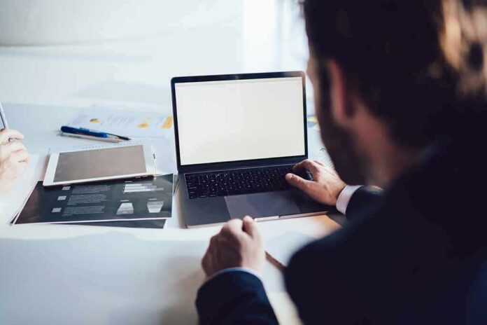 Person working at a laptop with blank screen on a desk