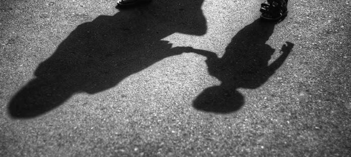 Shadows of an adult and a child holding hands on pavement